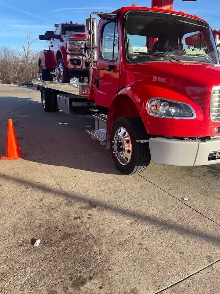 Red rollback tow truck carrying a pickup truck